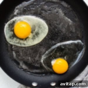 Two fried eggs beginning to cook in a frying pan, with butter bubbling around them.
