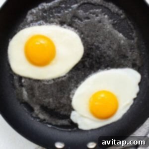 Two fried eggs continuing to cook in a frying pan, whites mostly set and edges still soft.