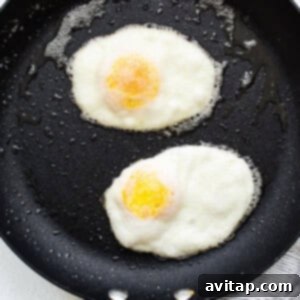 Two fried eggs flipped over in a frying pan, cooking on the second side to firm up the yolks.