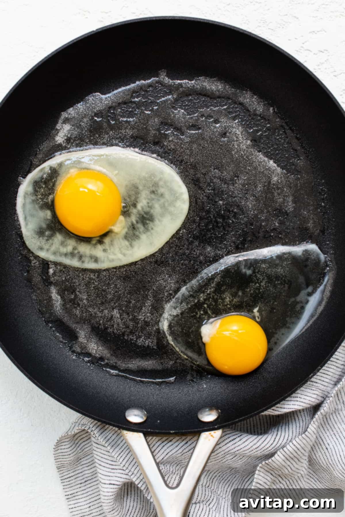Two over hard eggs sizzling gently in a non-stick skillet with melted butter.