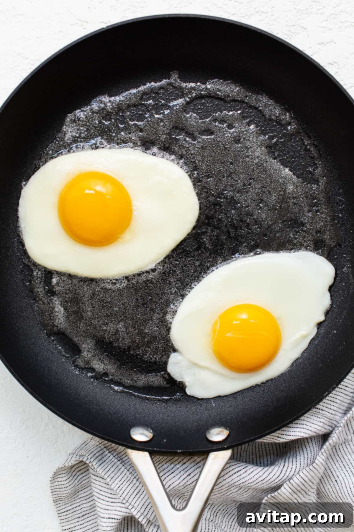 Two over hard eggs actively cooking in a skillet, showing the whites setting and steam rising.