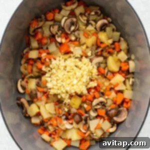 A mix of vegetables and minced garlic cooking in a Dutch oven.