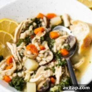 A bowl of chicken soup served with a fresh lemon slice and herbs.
