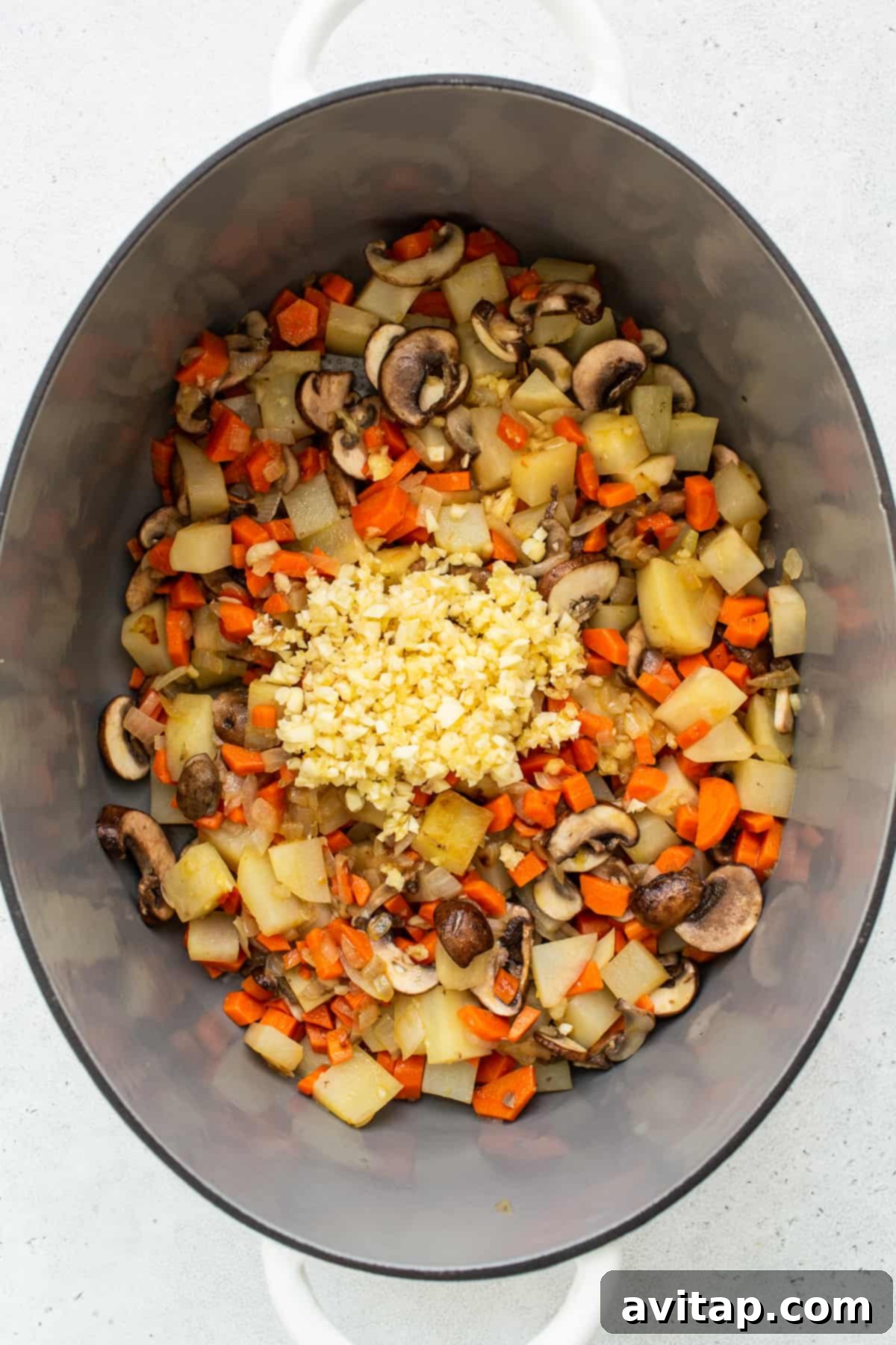 The Perfect Chicken Soup 3 Minced garlic and various fresh vegetables simmering in a Le Creuset Dutch oven, releasing aromatic flavors.