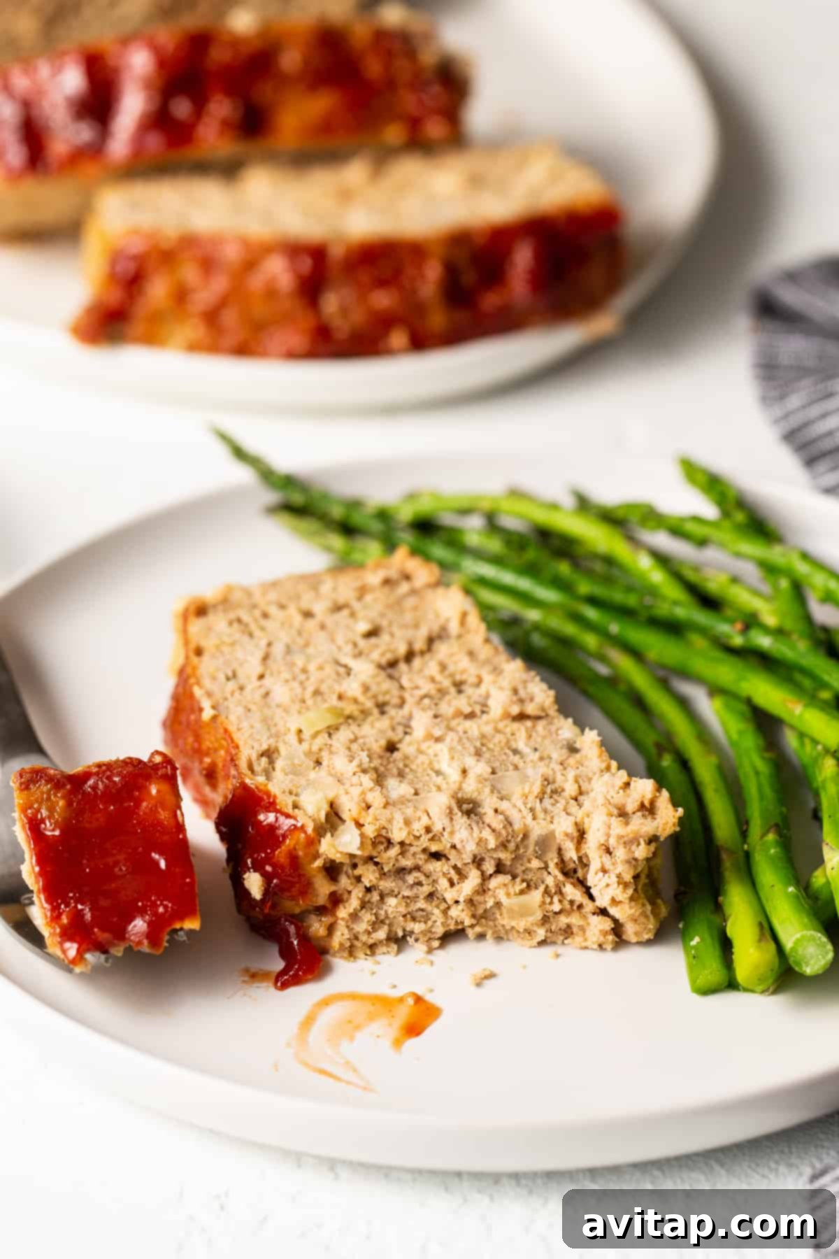 Perfectly cooked turkey meatloaf with a healthy side. A delectable slice of ground turkey meatloaf served on a plate with fresh roasted asparagus.