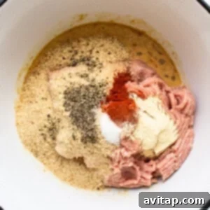 A bowl with ground meat and various spices, ready for mixing.