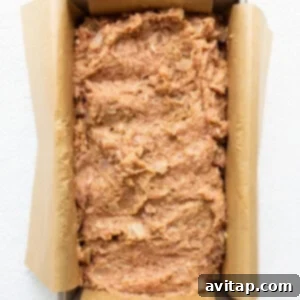 A loaf of bread in a pan on a white surface, shaped and ready.