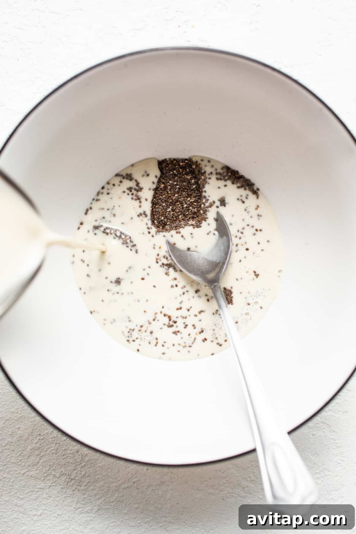 Chia seeds in a bowl with oat milk being poured over them.