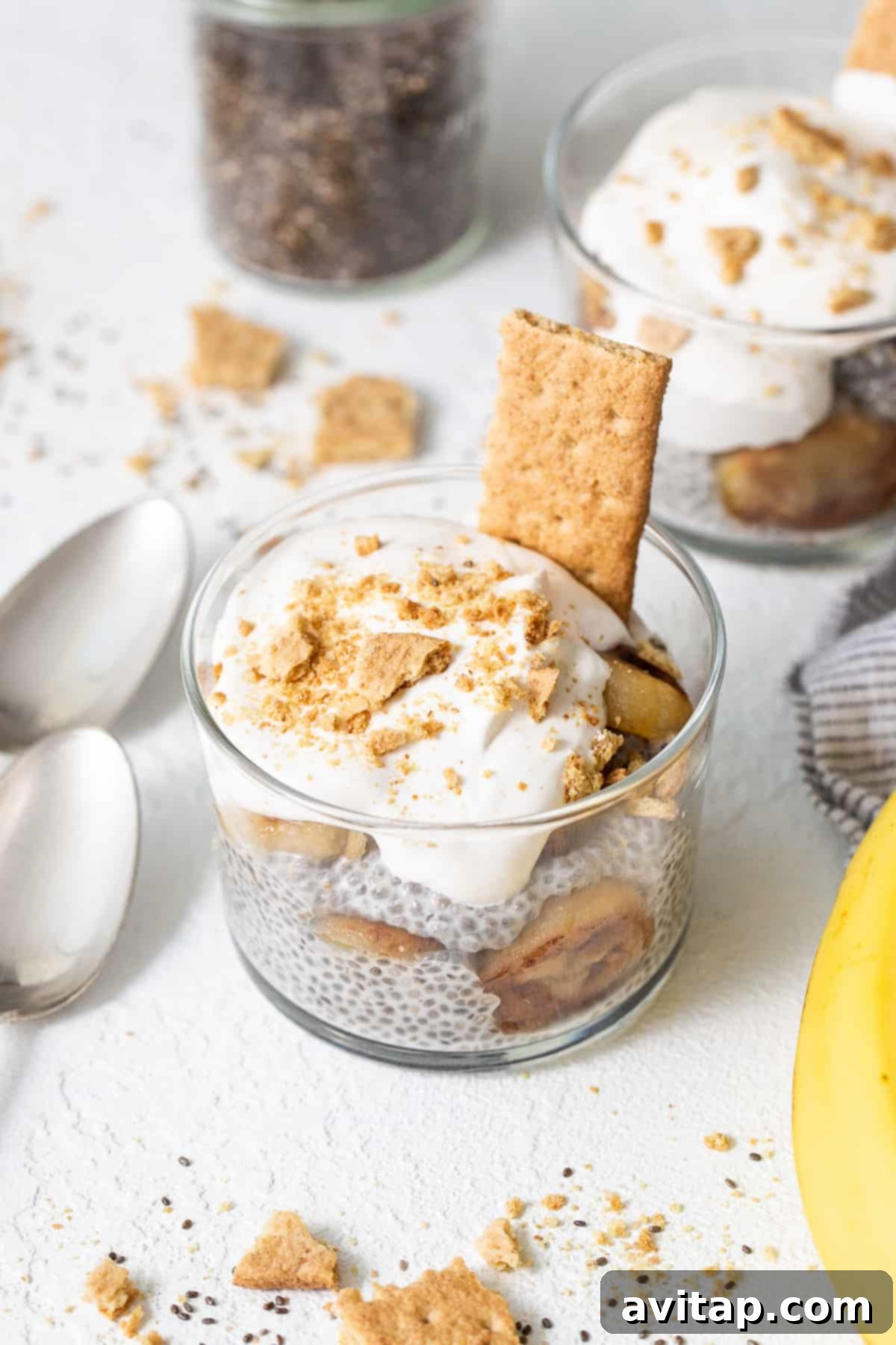 Five glasses of banana cream pie chia seed pudding, one topped with whipped cream and graham crackers, others with just banana.