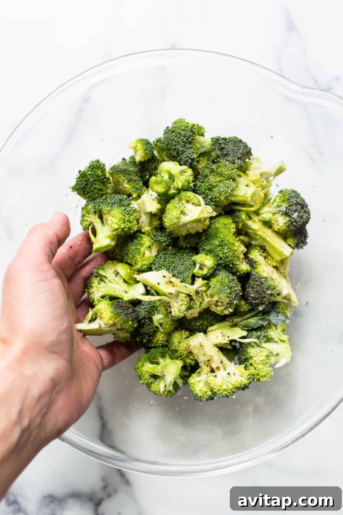 Broccoli florets in a bowl with seasoning and lemon.