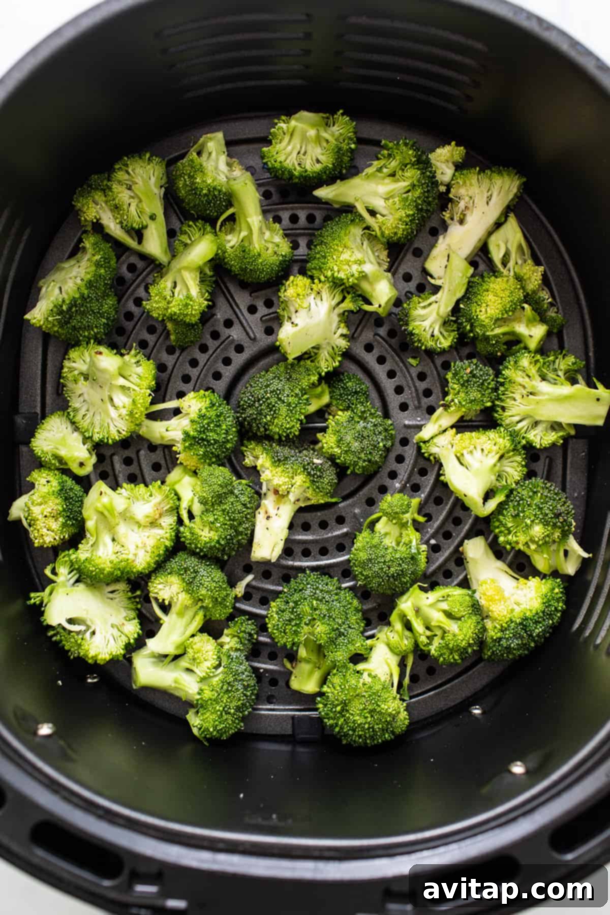 Broccoli florets being cooked in the air fryer basket.