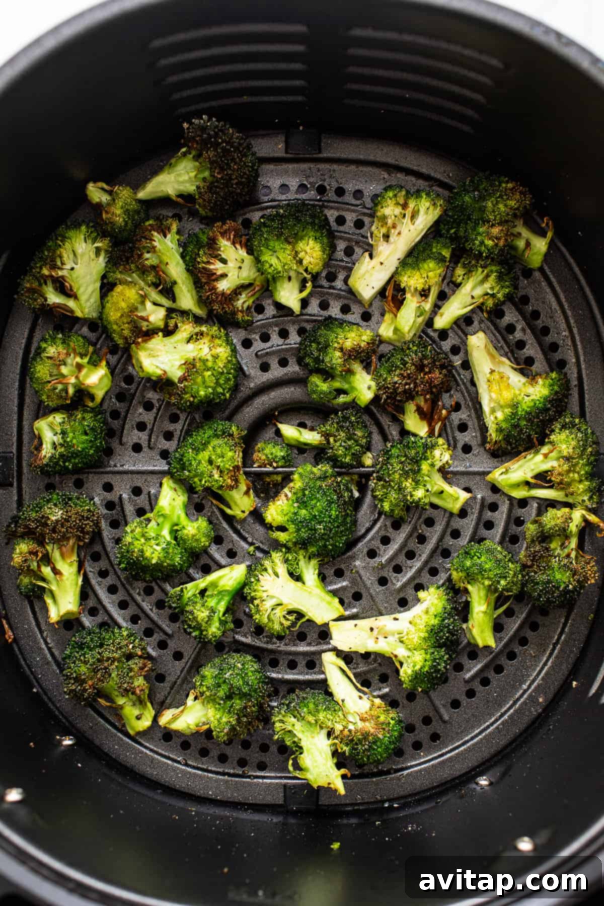 Crispy broccoli florets cooking in an air fryer.