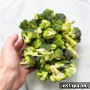 A person holding broccoli in a glass bowl.