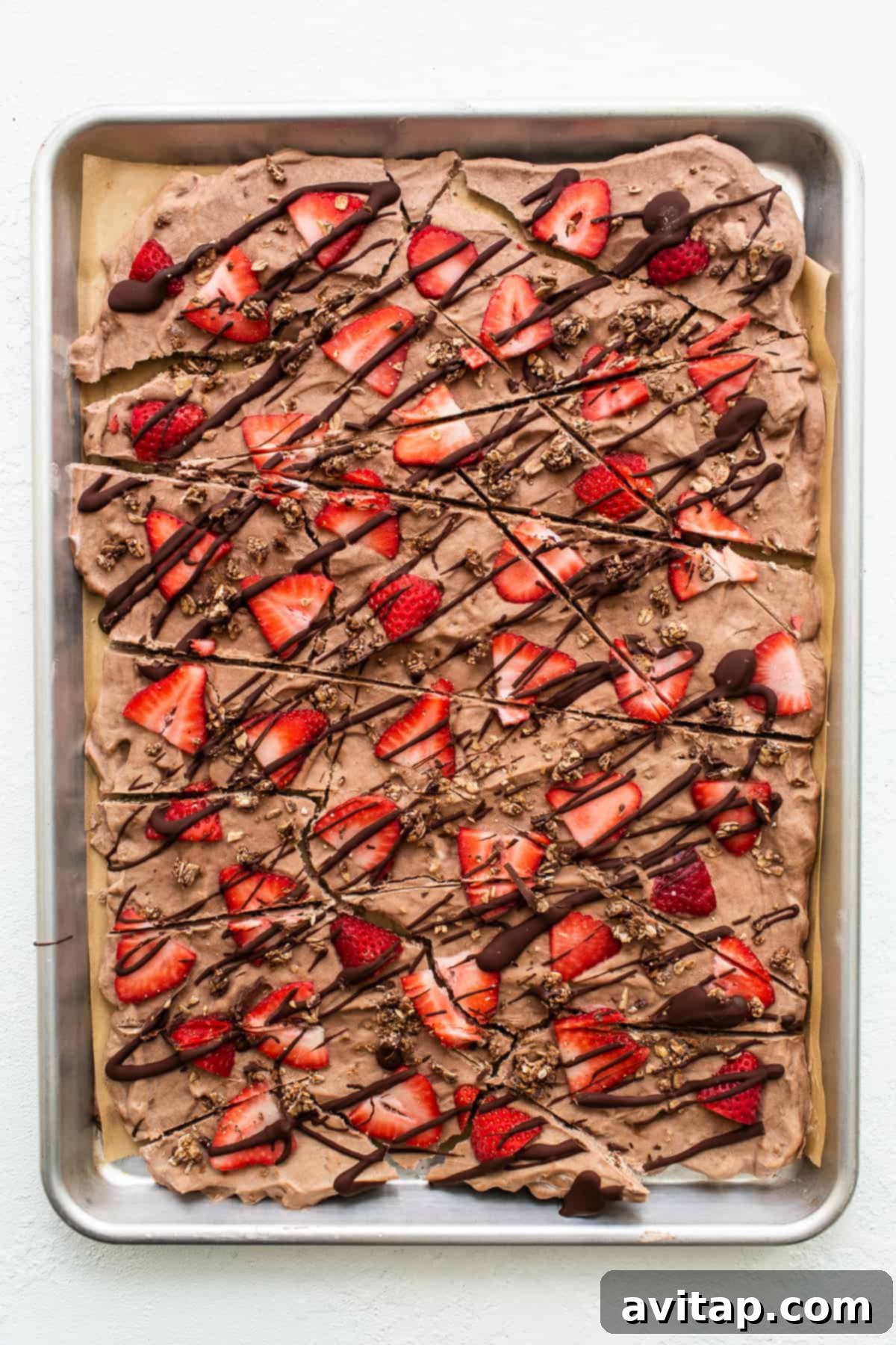 A sheet of chocolate strawberry frozen yogurt bark, beautifully finished with strawberries and chocolate drizzle, ready to be broken into pieces.