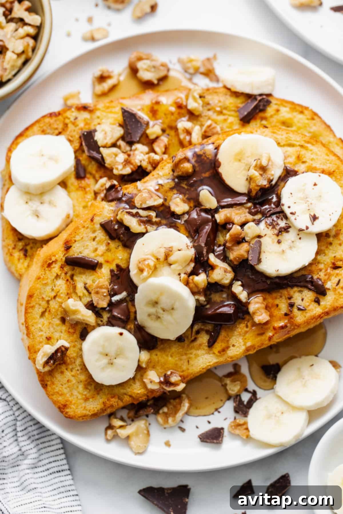 A stunning close-up of Air Fryer Chunky Monkey French Toast, beautifully garnished with melted chocolate, crunchy walnuts, and fresh banana slices, ready to be enjoyed.
