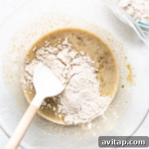 Decadent Bananas Foster Muffins 8 Adding dry ingredients to wet ingredients in a mixing bowl for muffin batter.