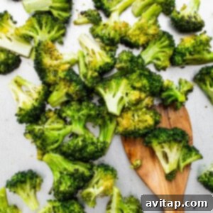 Chopped broccoli on a white plate with a wooden spoon, showing roasted texture.