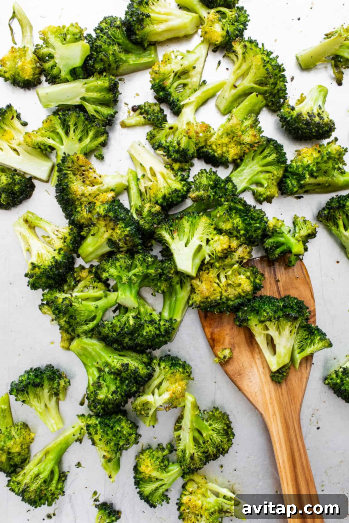 A serving of roasted broccoli being scooped from a pan with a spatula.