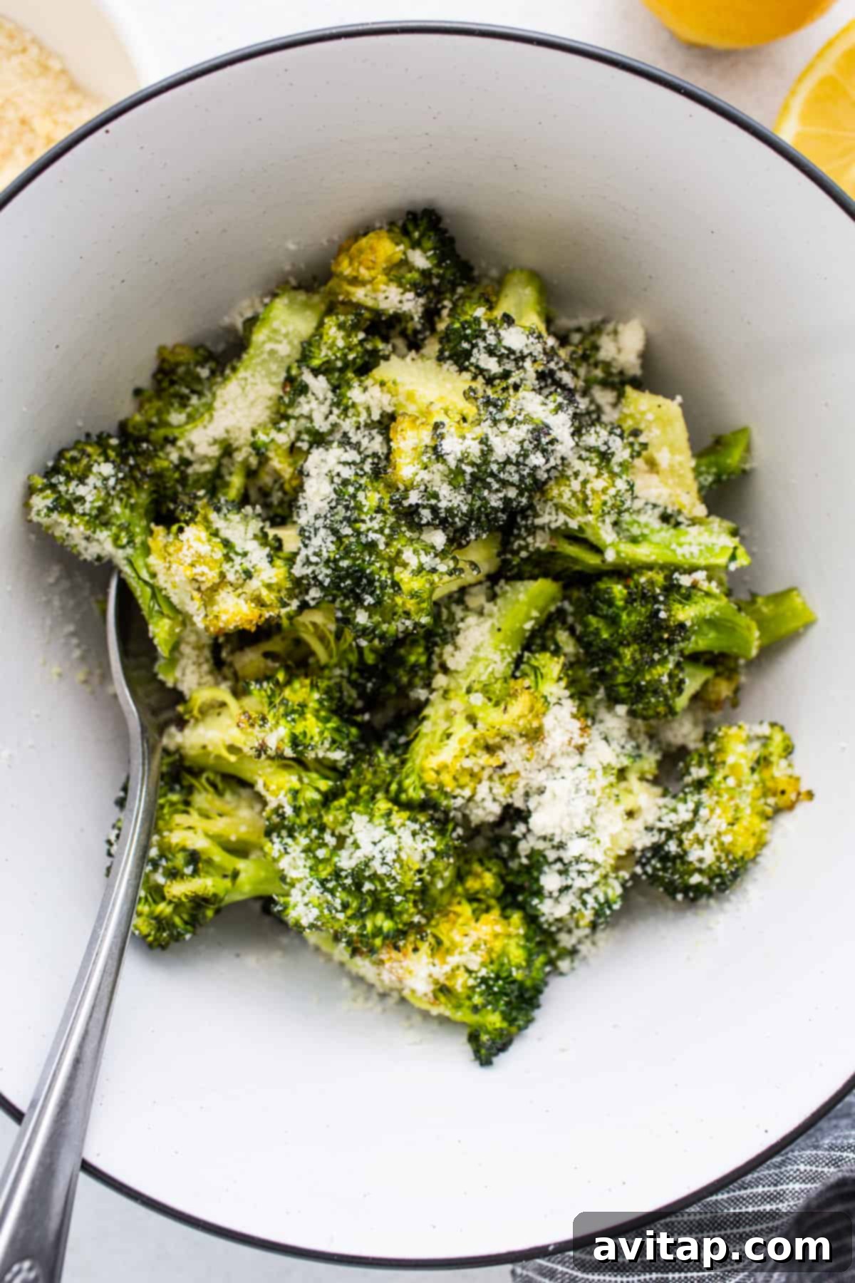 A close-up of roasted broccoli florets topped with a generous sprinkle of grated parmesan cheese, served on a plate.