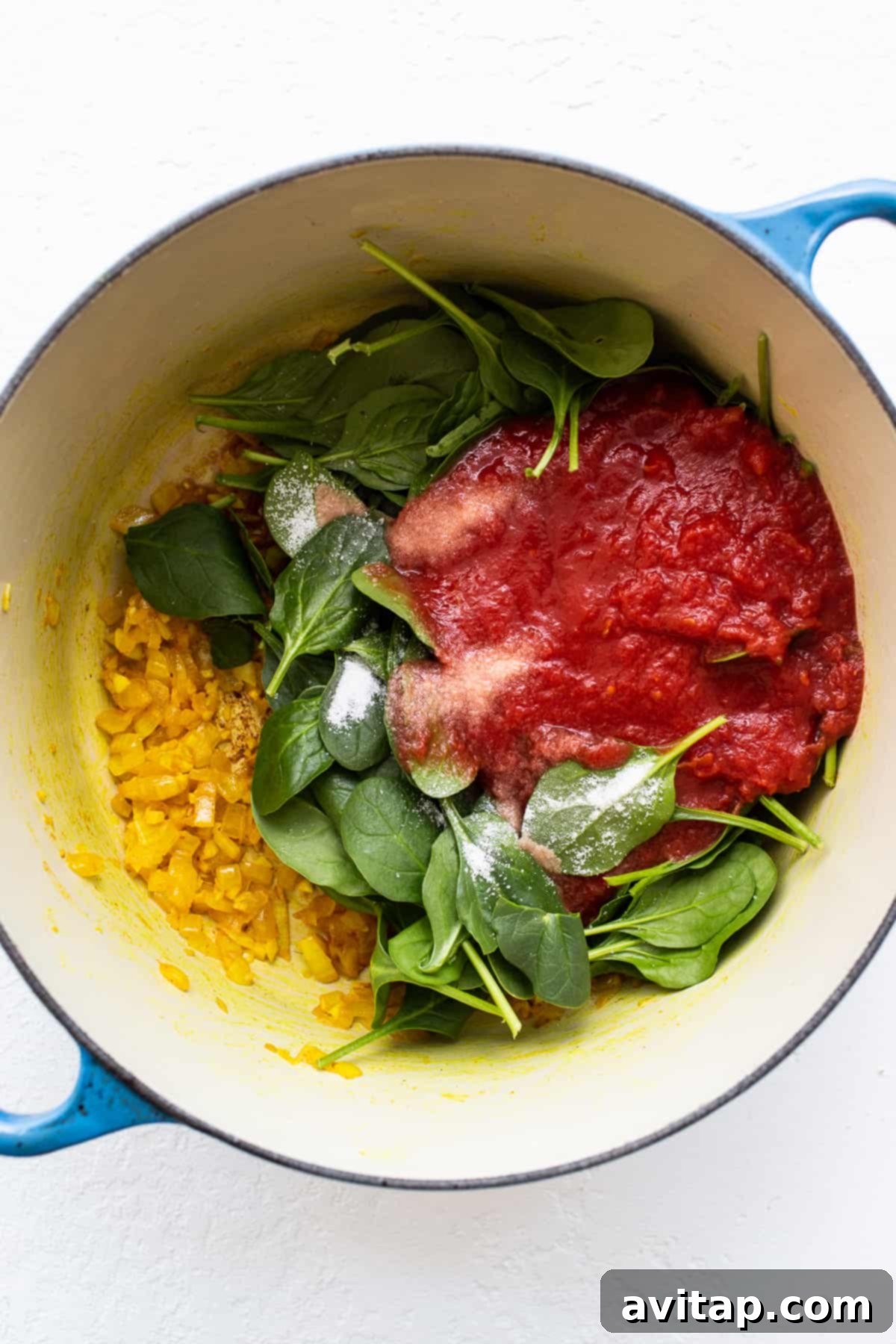 Fresh ingredients beginning to simmer in a Dutch oven. Spinach, crushed tomatoes and onions in a dutch oven.