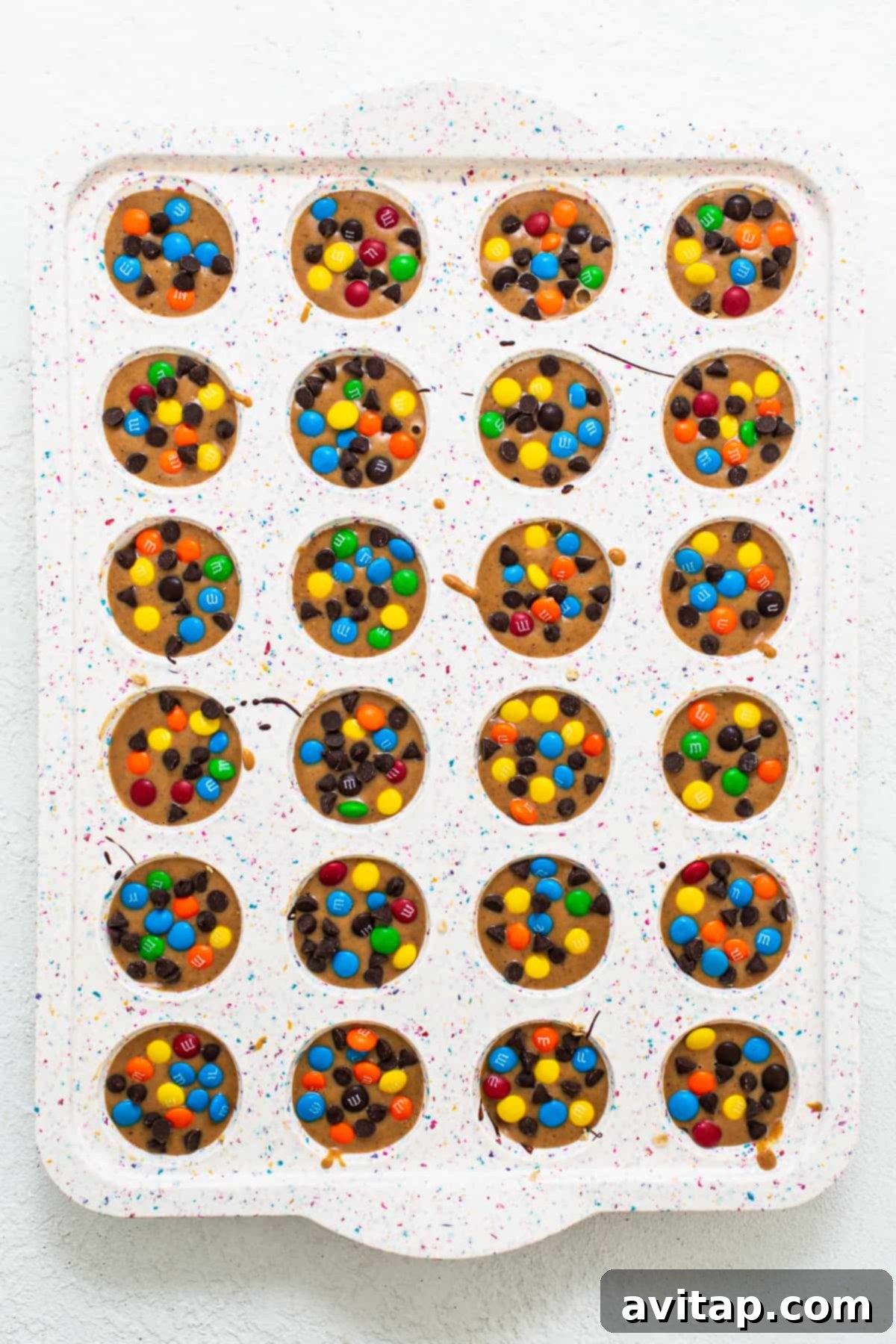 Monster cookie oat cups neatly arranged in a mini muffin tin, ready to be chilled.