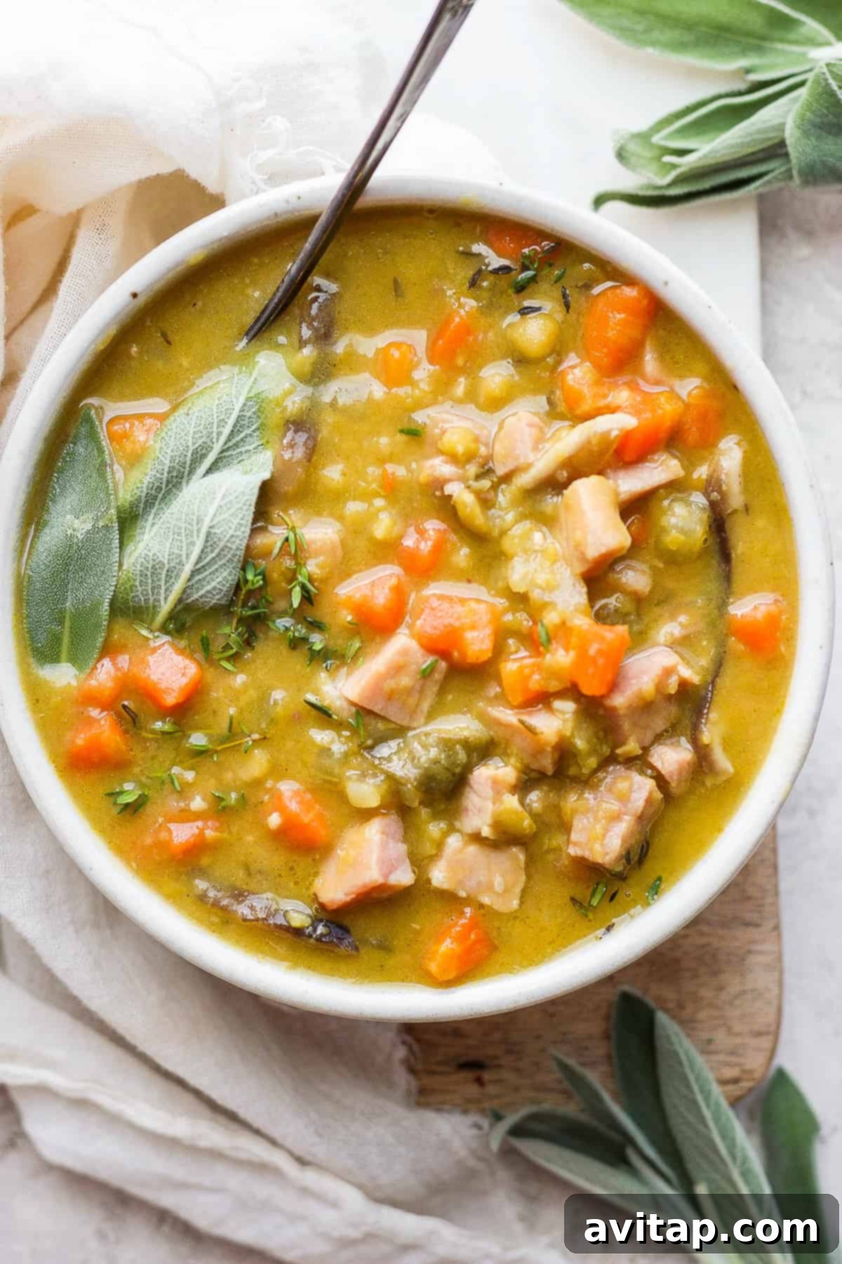 A comforting bowl of split pea soup with ham, garnished with a sprig of fresh thyme, and a spoon resting in the bowl, inviting a taste.