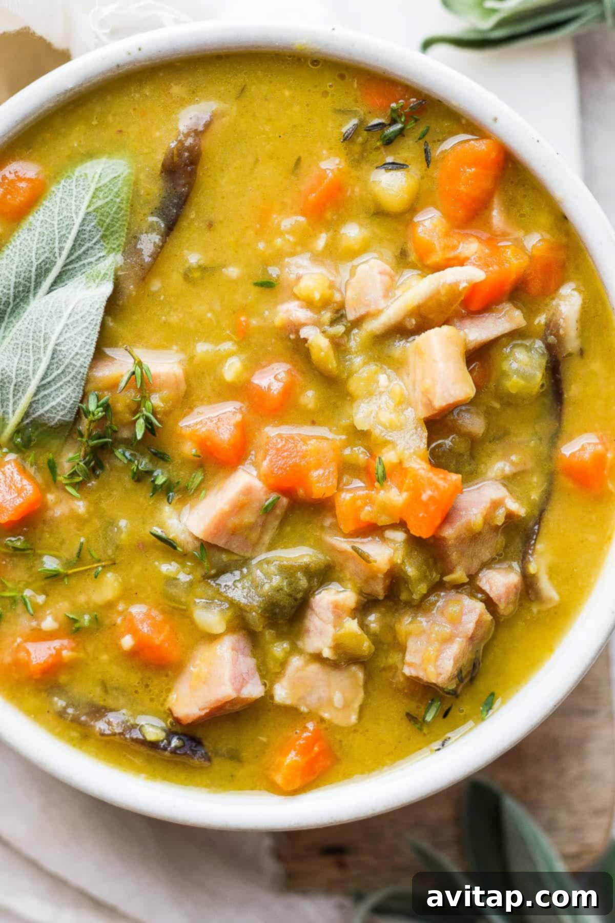 A beautifully presented bowl of creamy split pea soup with ham, garnished with fresh herbs and a drizzle of olive oil, ready to be enjoyed.
