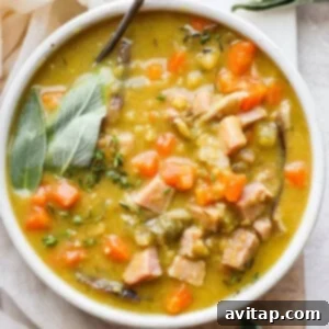 A comforting bowl of split pea soup with ham, garnished with a sprig of fresh thyme, and a spoon resting in the bowl, inviting a taste.