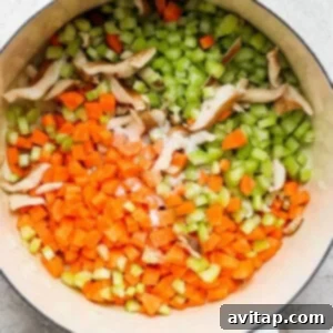 A pot with carrots, celery, and mushrooms beginning to soften.