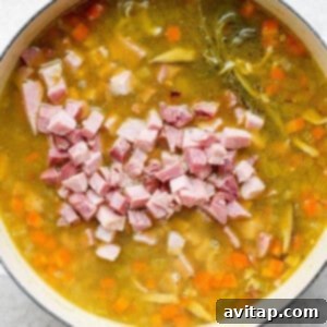 A pot of soup with ham and carrots, simmering.