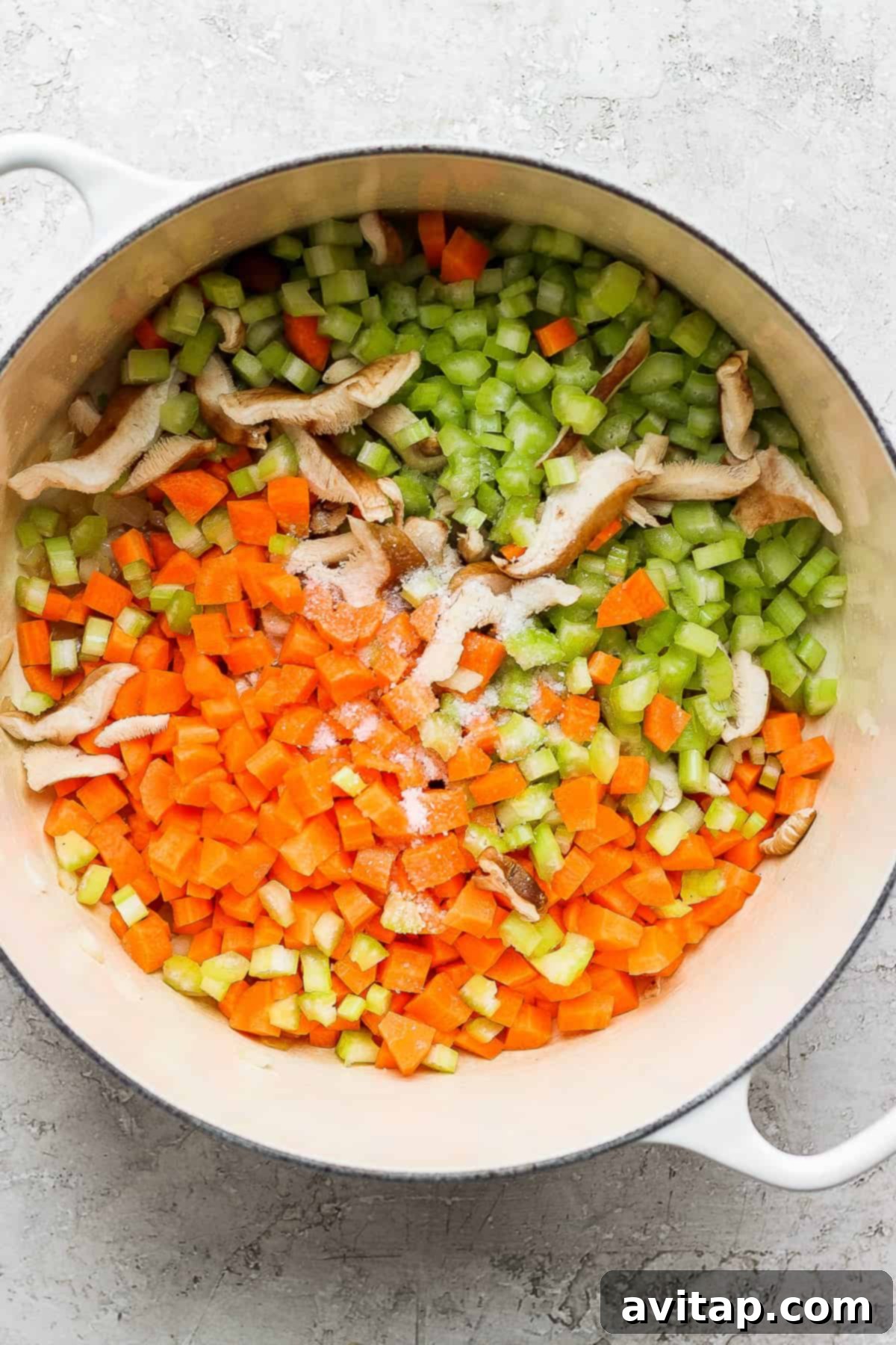 Diced carrots, celery, and mushrooms sautéing in a Dutch oven with onions and garlic, releasing their aromas and softening.