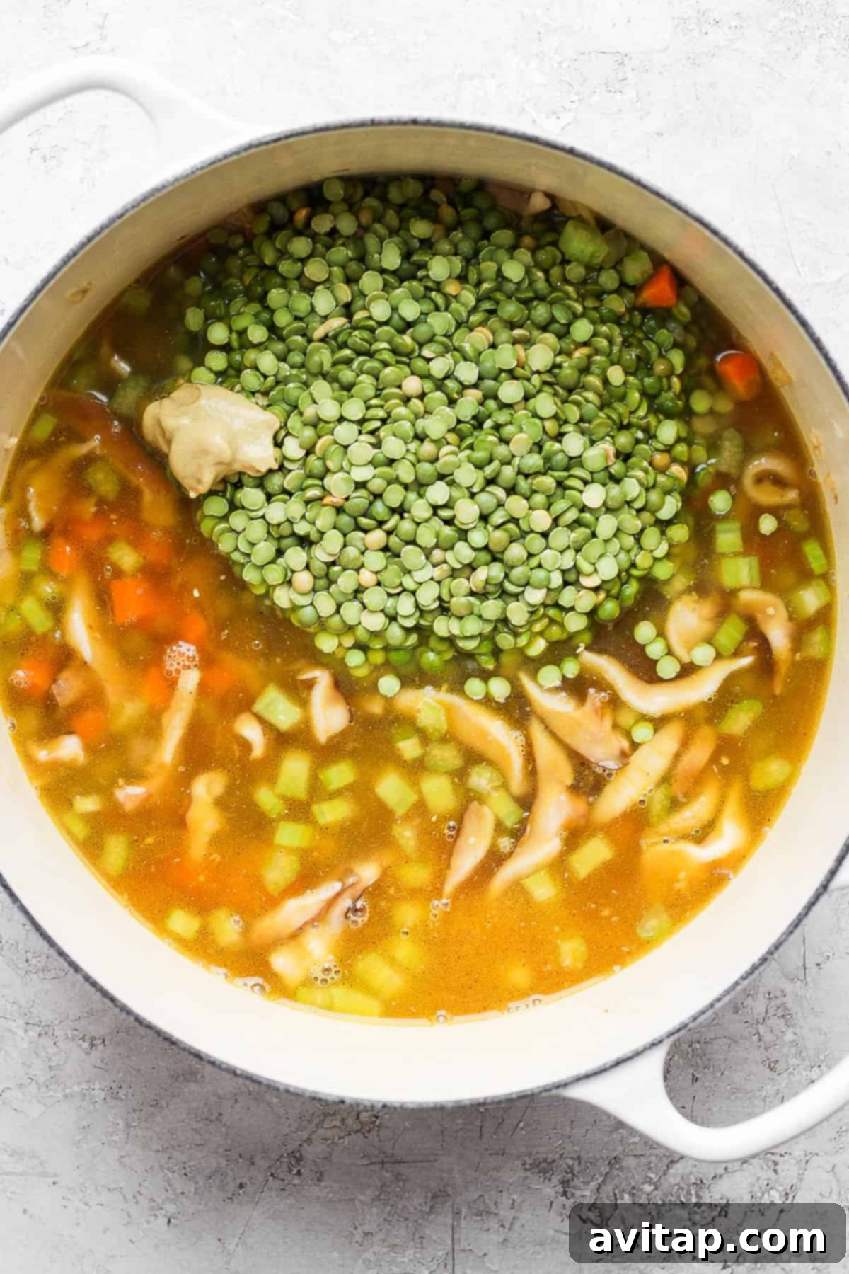 Split peas and various vegetables simmering in a Dutch oven with savory broth, with fresh herbs submerged for flavor.