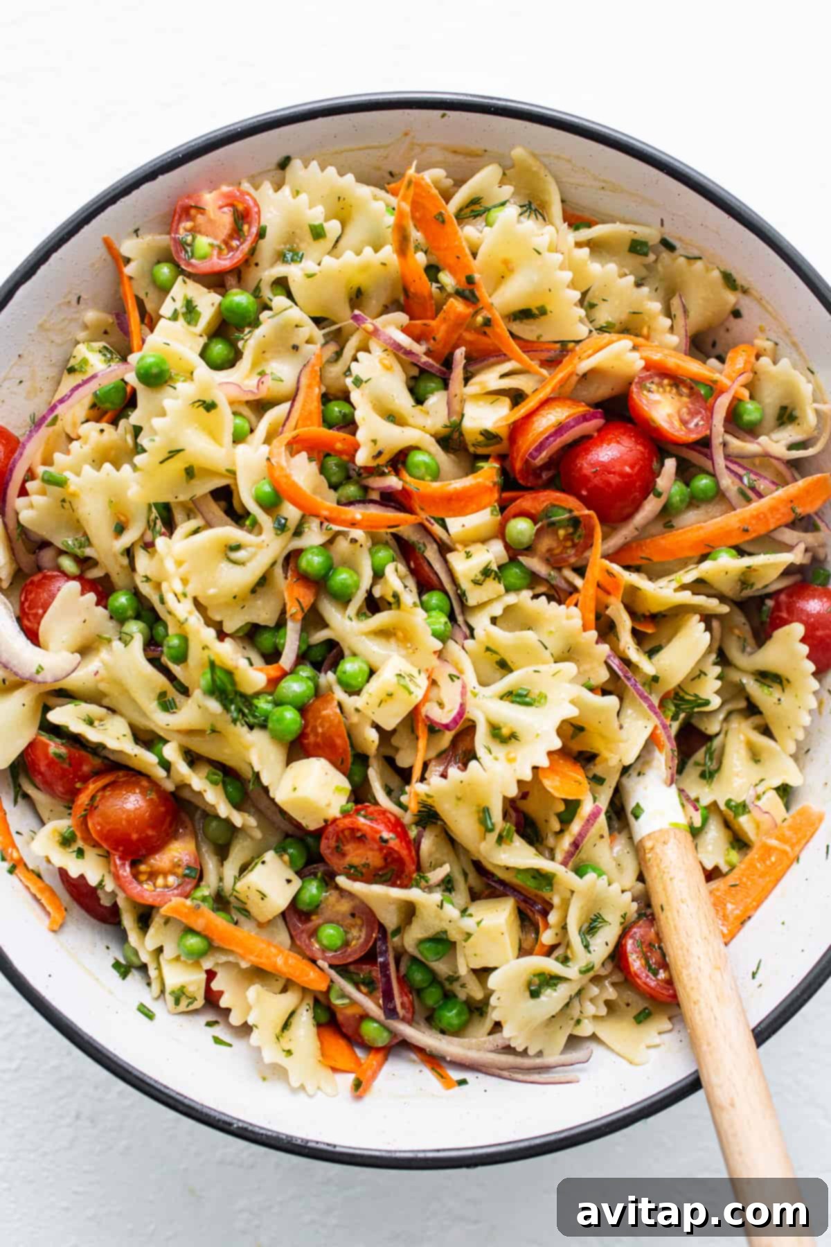 A large ceramic bowl filled with colorful bow tie pasta salad, mixed with vegetables and a creamy dressing. A serving spoon rests in the bowl, inviting a taste.