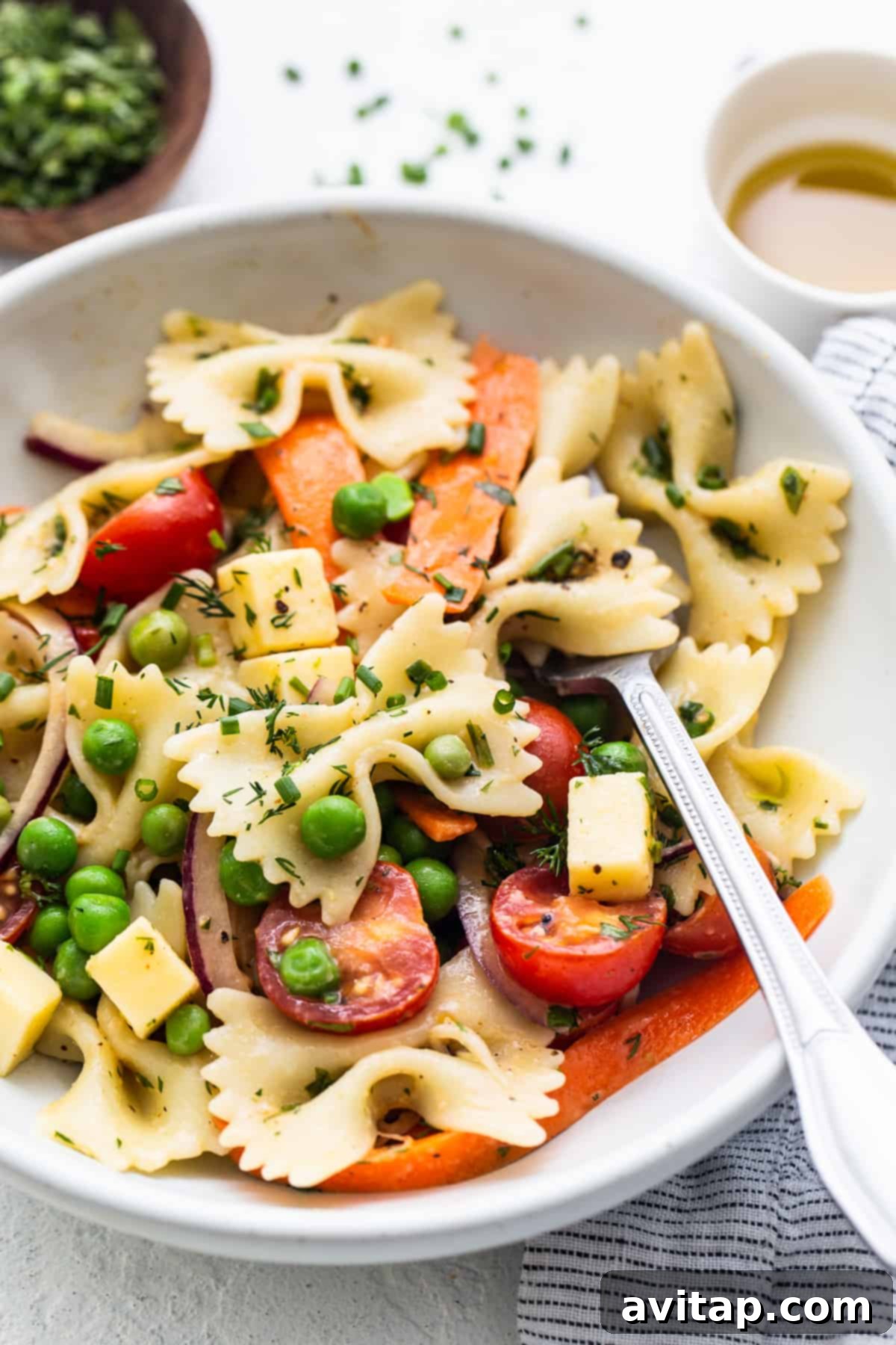 A single serving of bow tie pasta salad in a small white bowl with a fork, showing the vibrant mix of pasta, vegetables, and creamy dressing.