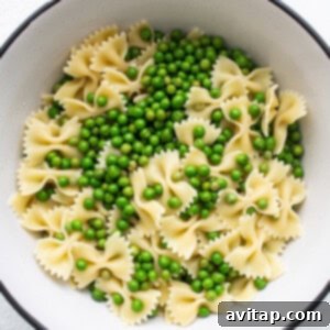 A bowl of cooked bow tie pasta with blanched English peas.