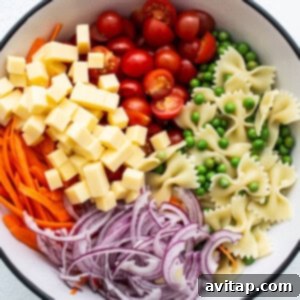 A bowl of pasta salad with colorful carrots, peas, and cheese mixed in.