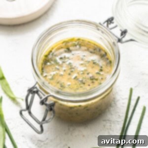 A glass jar containing a vibrant green sauce, with a whisk resting beside it, on a clean white background.