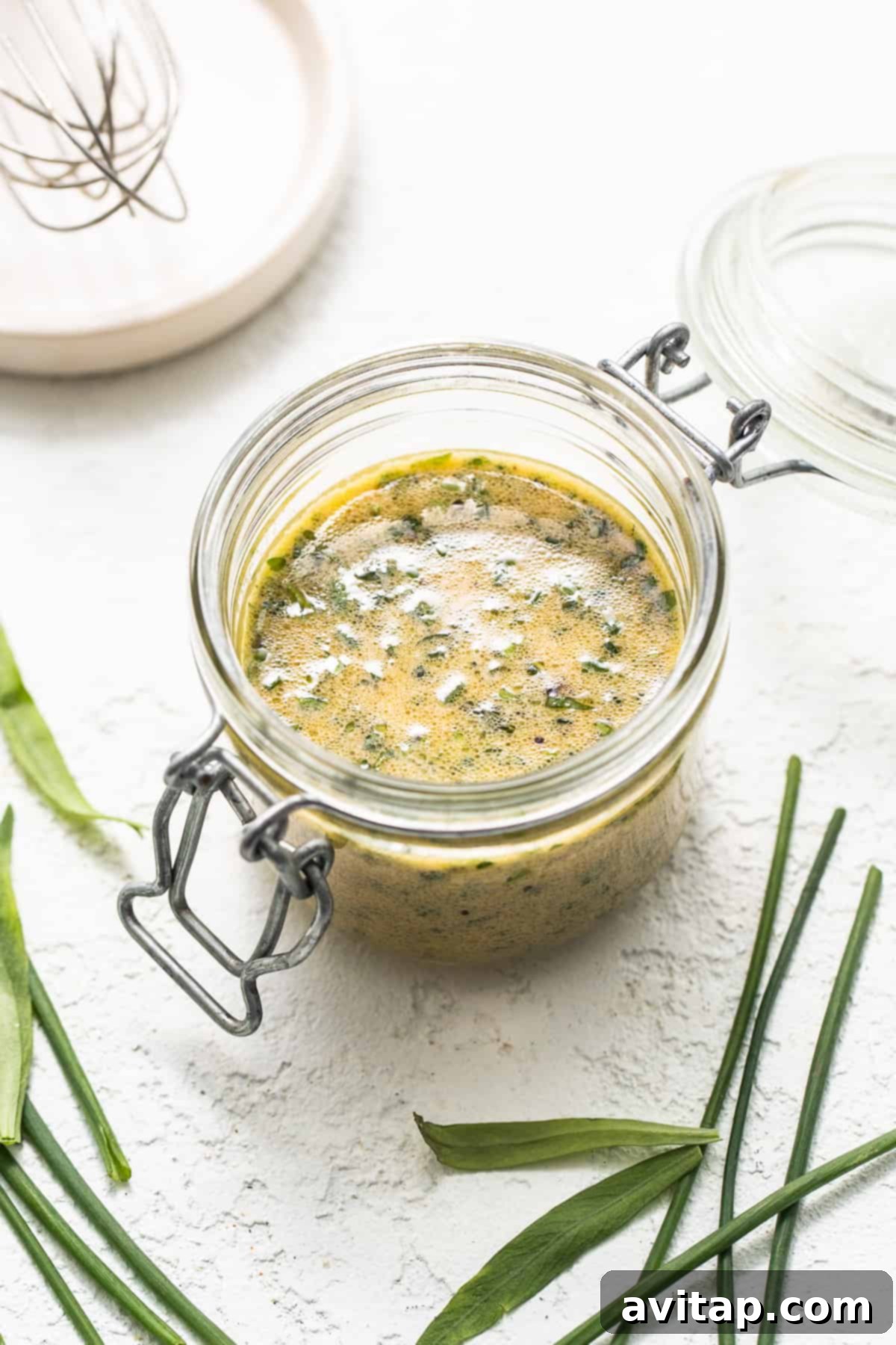 A glass jar filled with a creamy, light green homemade hummus dressing, set on a clean white surface, highlighting its smooth texture.