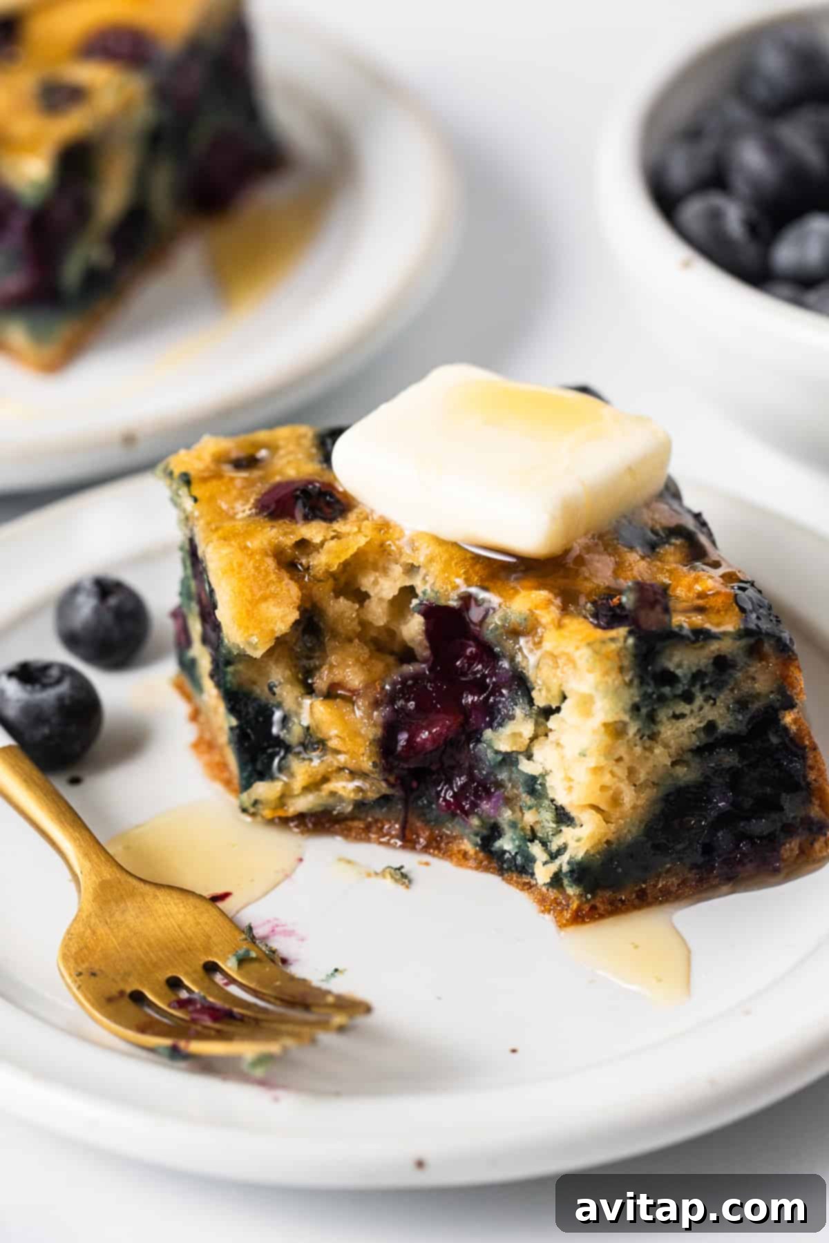 A freshly baked blueberry breakfast cake, golden brown and topped with juicy blueberries, ready to be sliced and served with a cup of coffee.