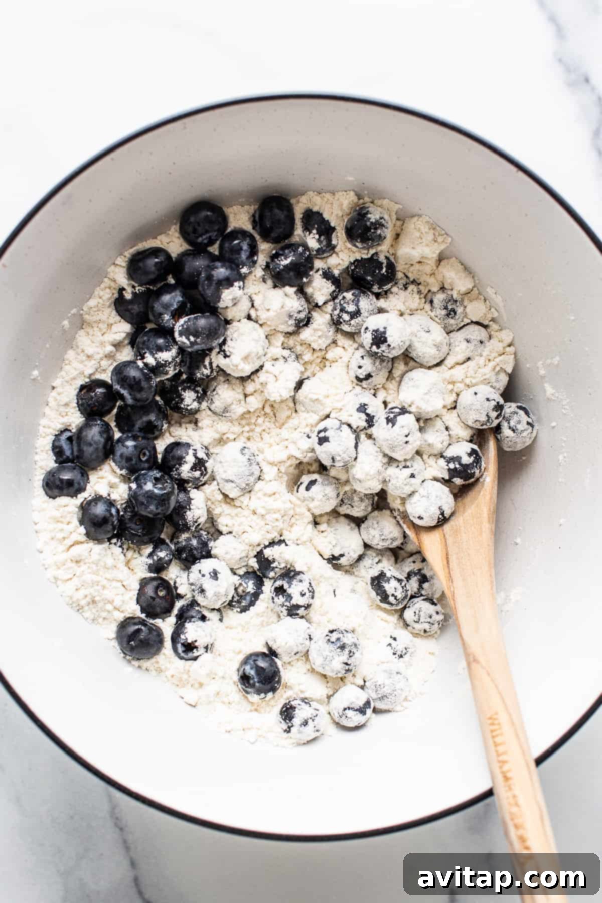 Close-up of the light and fluffy batter for blueberry breakfast cake, showing fresh blueberries gently folded in before baking, ready for the pan.