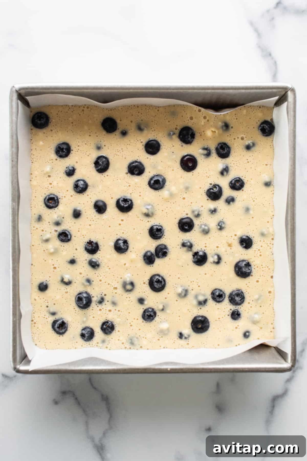 A top-down view of the freshly baked blueberry breakfast cake, golden brown and glistening, sliced into perfect squares on a wire cooling rack.