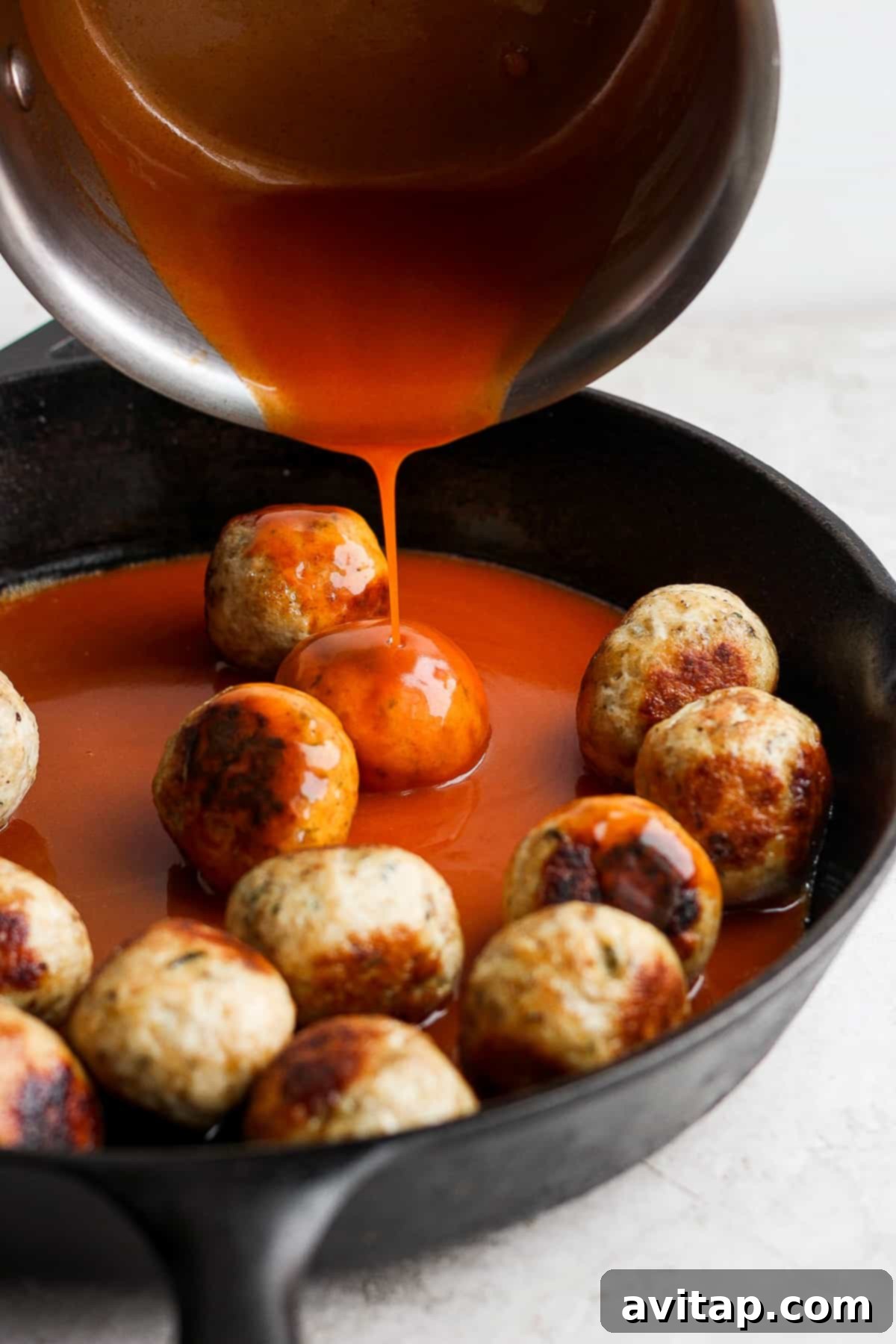 pouring buffalo sauce on top of meatballs.
