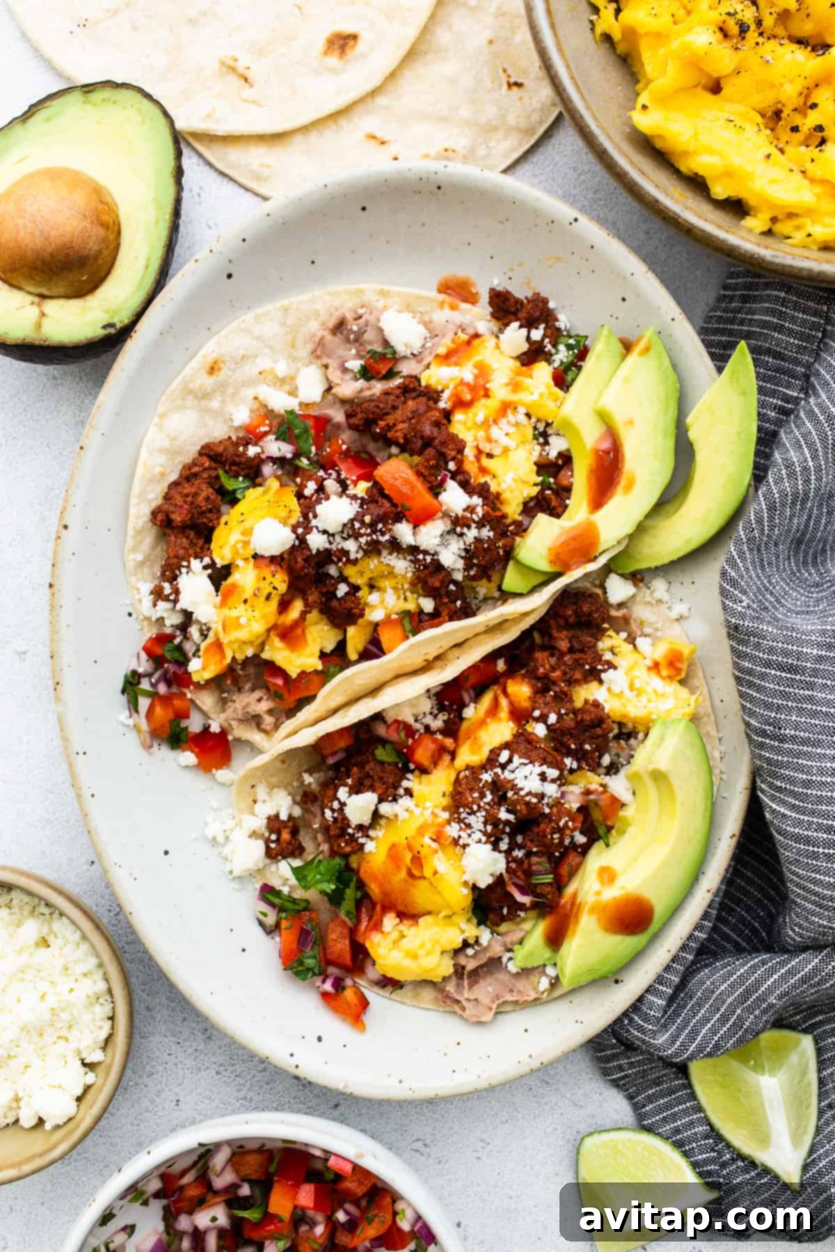 Two breakfast tacos with eggs, chorizo, and toppings on a white plate, ready to be enjoyed.