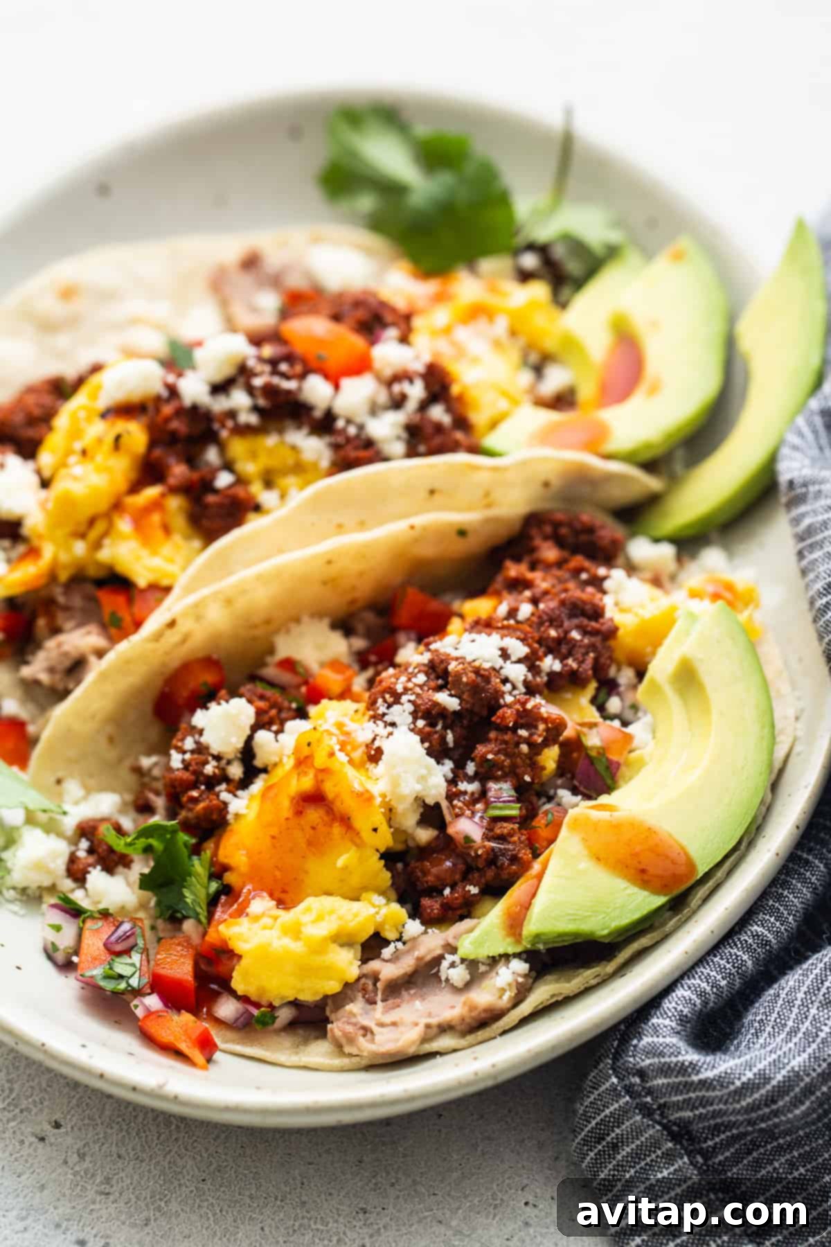 A pair of perfectly assembled breakfast tacos on a clean white plate, garnished with cilantro.
