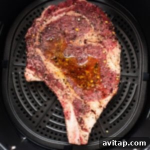A steak cooking in an air fryer basket, with visible browning.
