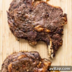 Two perfectly cooked steaks resting on a wooden cutting board before slicing.