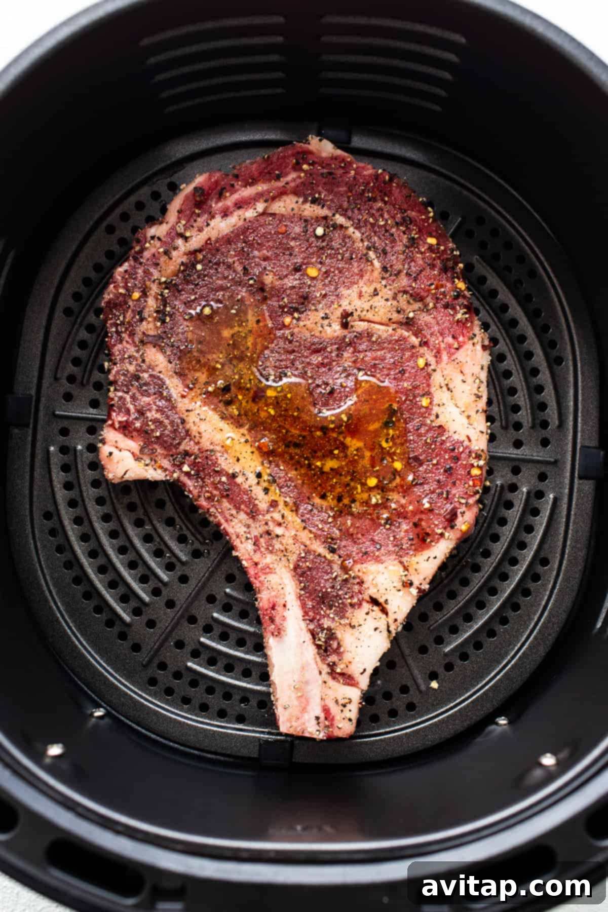 A steak sizzling and browning in the basket of an air fryer.