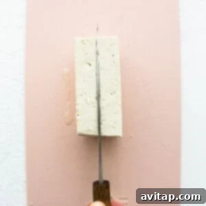 A person cutting a piece of tofu on a pink surface.