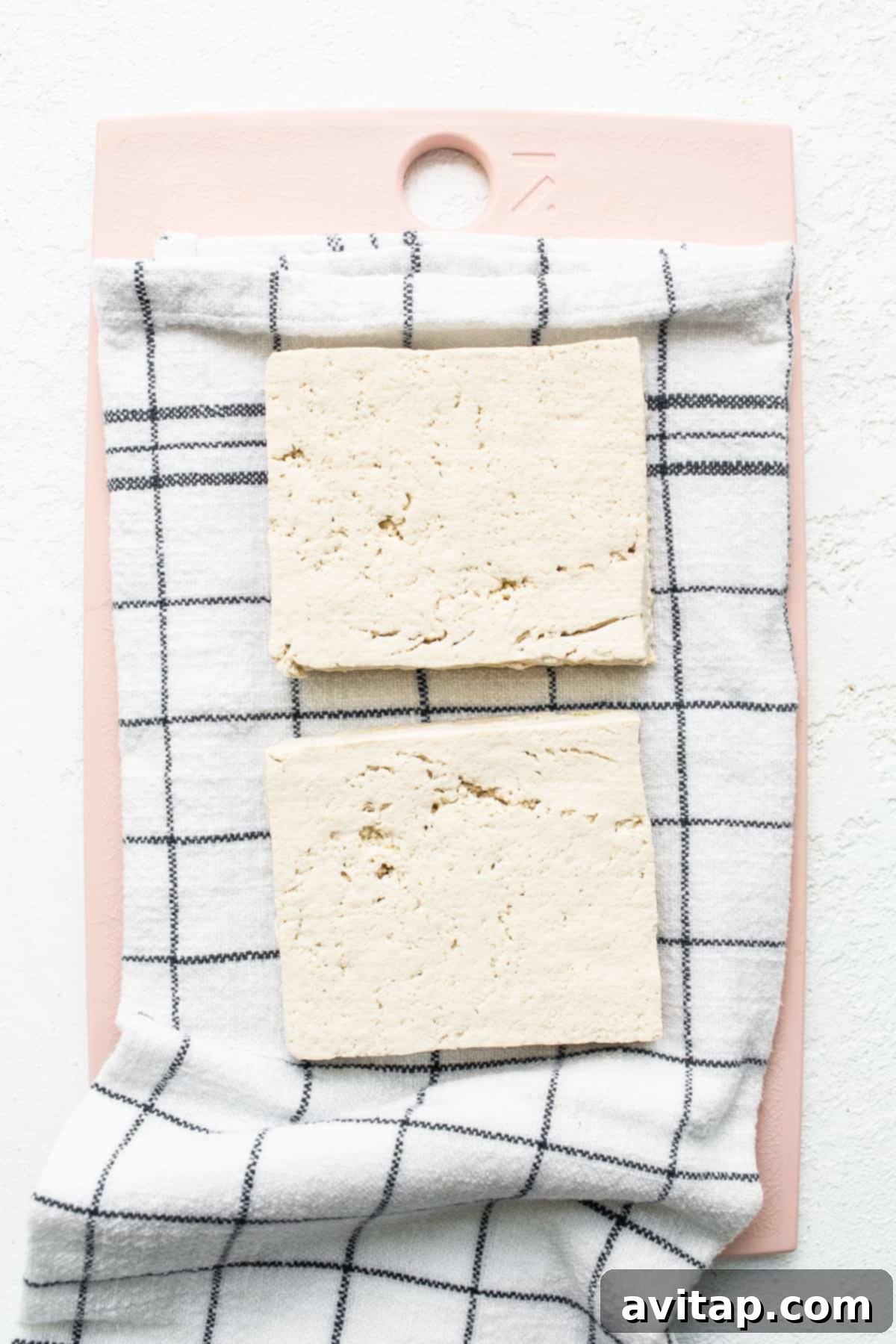 A block of extra-firm tofu sliced on a cutting board, ready for pressing.
