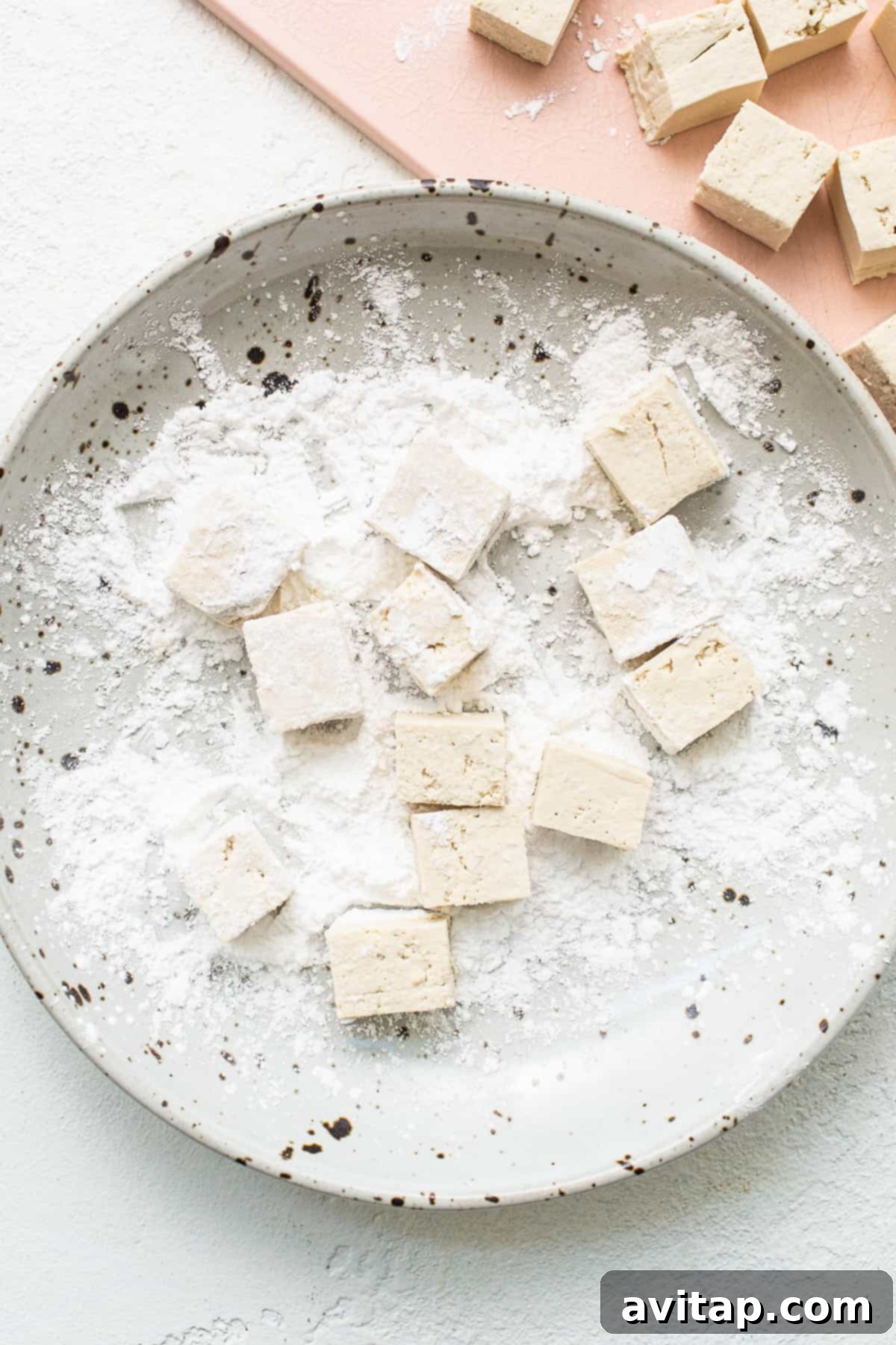 Tofu cubes being tossed with cornstarch and salt in a bowl.